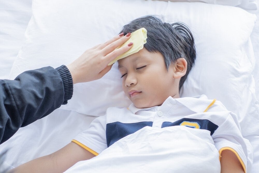 A hand wipes an Asian male child’s forehead to help lower his fever instead of wrapping him up in heavy blankets, a Filipino myth.