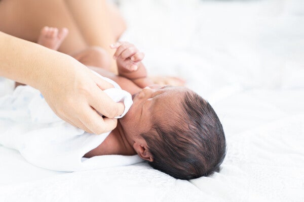 Close-up of a parent’s hand gently dabbing a baby's face with a soft, damp cloth to prevent newborn facial rash.