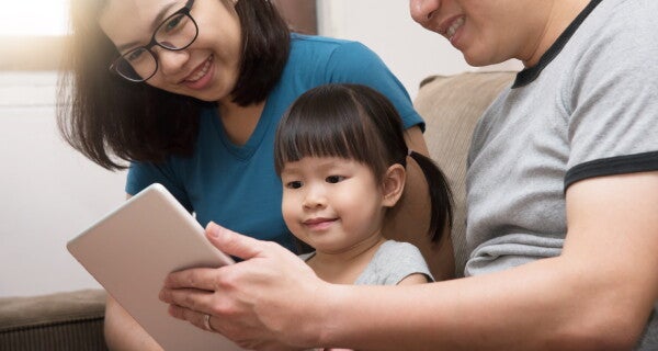A happy Asian family sitting and using a tablet to watch animated Bible clips.