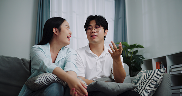 Low angle view of young Asian couple talking happily on a sofa at home