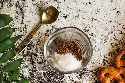 Photo of a glass with instant coffee and sugar in it, ready on a table with a teaspoon beside it