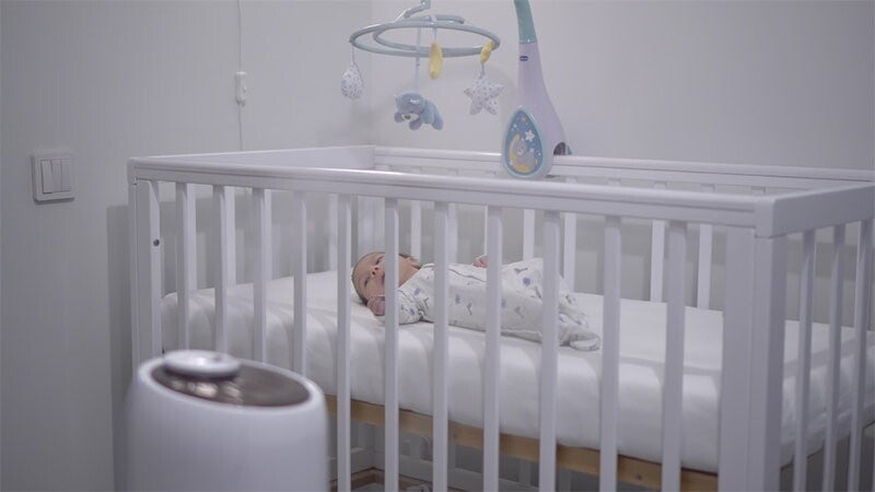 Photo of a newborn lying in a crib with a humidifier in the foreground.