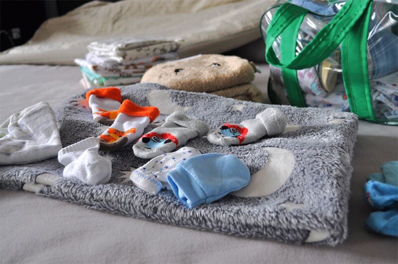 Photo of newborn socks, booties, hats, blankets, diapers, and bag for the maternity hospital in bed