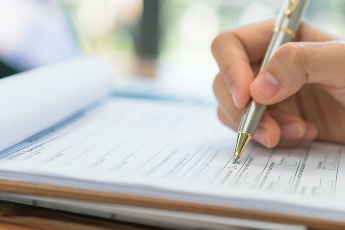 Close-up pic of a hand holding a pen over an application form for a solo parent ID.