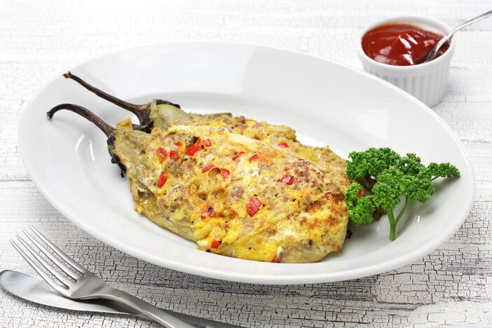 Photo of tortang talong on a white plate with utensils and ketchup on a sauce dish on the side. 