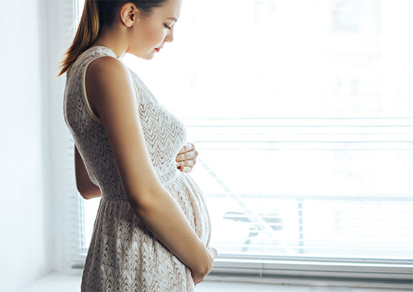 A pregnant Asian woman in her second trimester wearing an empire cut dress.