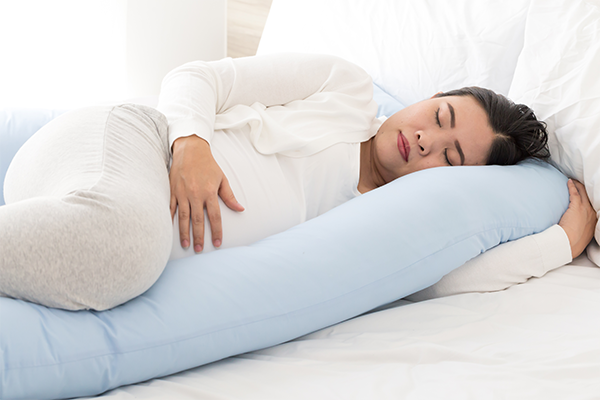 A pregnant Asian woman sleeping on her left side with a body pillow.