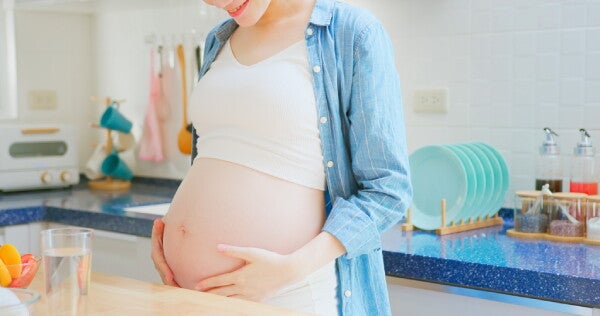 Cropped image of a woman holding her pregnant belly by the kitchen counter; nutrition concept.