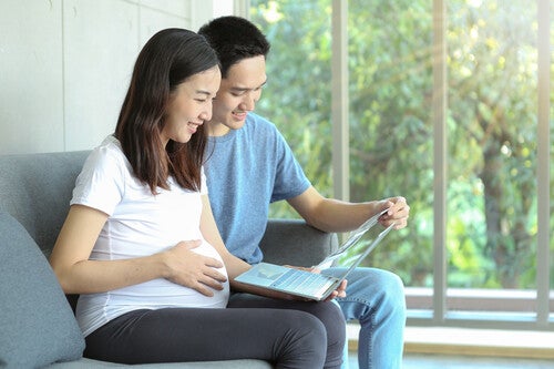 Pregnant Asian couple looking at their laptop for web-based pregnancy apps