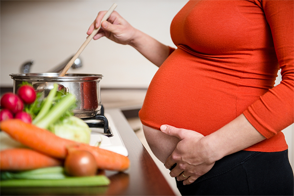 Pregnant woman holding her belly while cooking