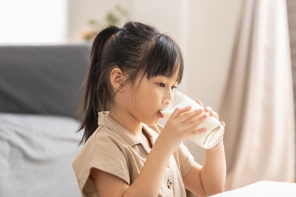 Little preschooler girl drinking a glass of milk at home.