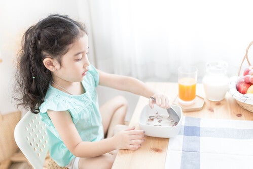 Preschooler Asian girl eating a bowl of cereal with milk, and a glass of orange juice and pitcher of milk on the side