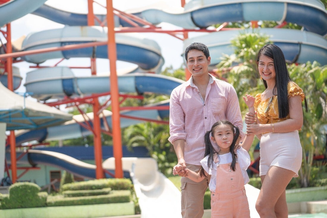 A young Asian couple with their daughter holding hands at a water park.