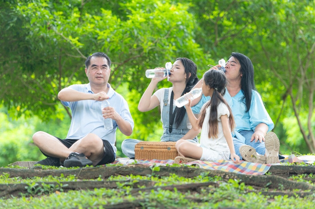 An Asian family staying hydrated and resting in shade during a family outing. 
