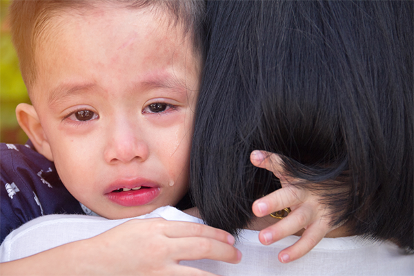 Sad young preschooler with his head on his mom’s shoulder with tears in his eyes