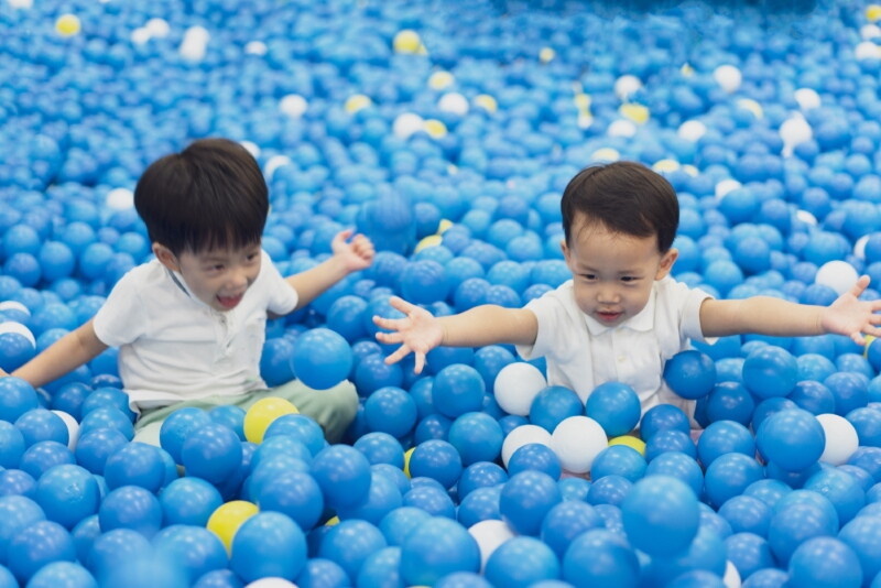 Two Asian brothers in healthy bmi range play in a plastic ball pit. 