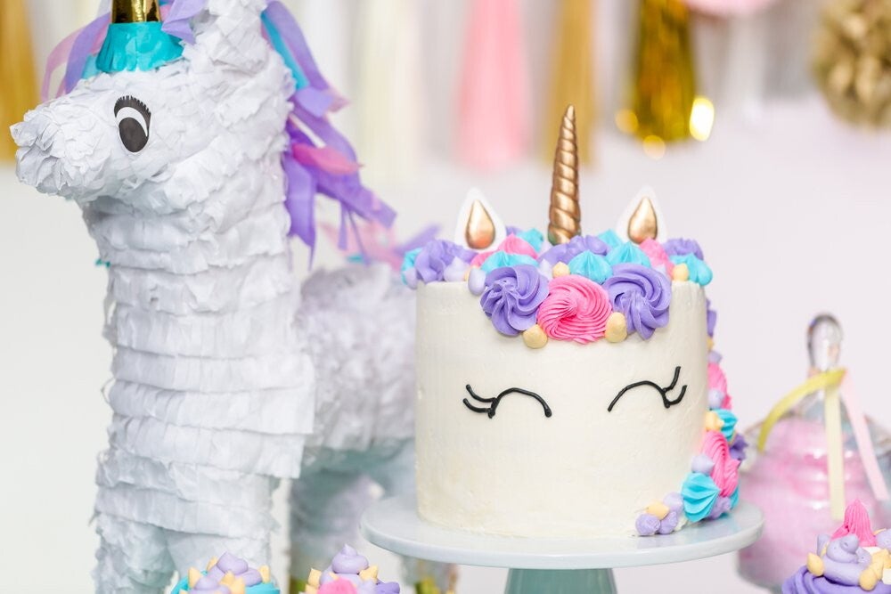 A birthday party table with a unicorn cake and a unicorn centerpiece. 