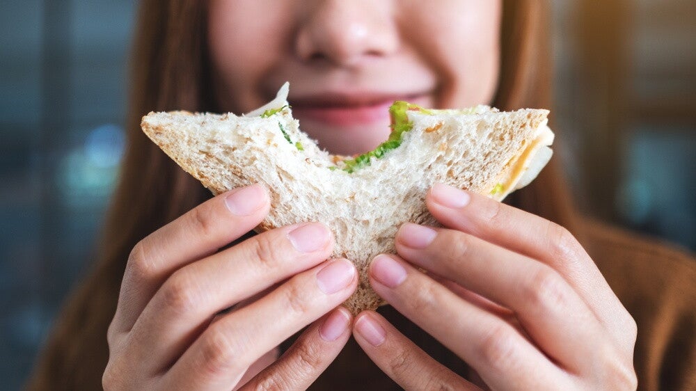 Closeup of woman holding up half a sandwich she took a bite of.