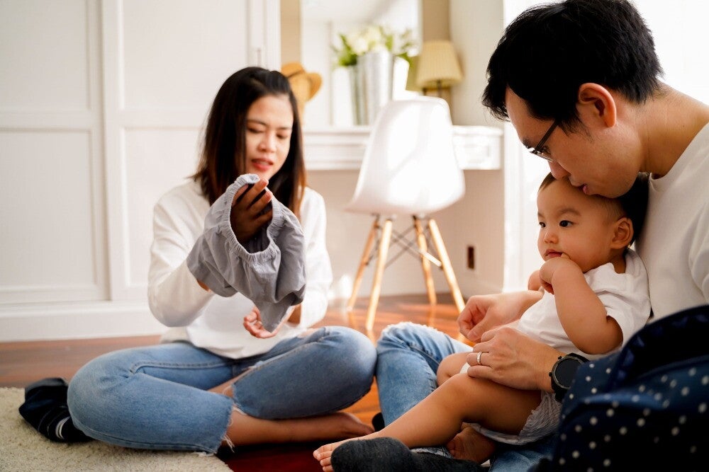 Young Asian couple sits on the floor as they dress their baby.