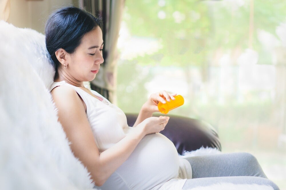 Asian pregnant woman takes her doctor-prescribed folic acid supplement.