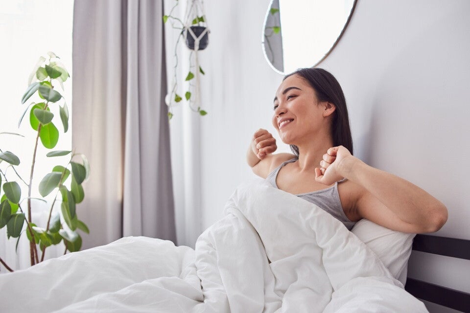 A young Asian woman sitting up and stretching in bed in the morning.