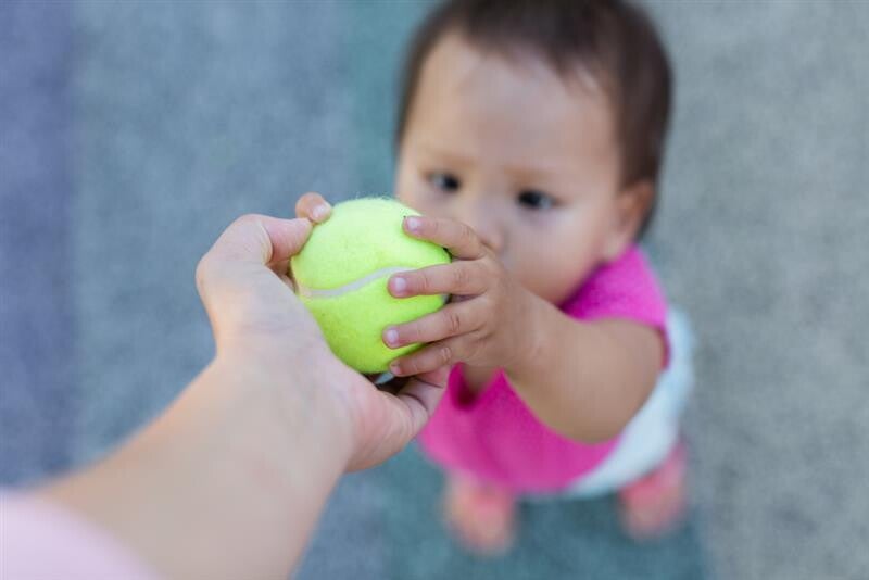 sian toddler girl hands a tennis ball to her parent.  