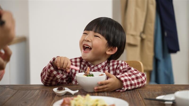 Close-up pic of a cute Asian little boy laughing while eating. 