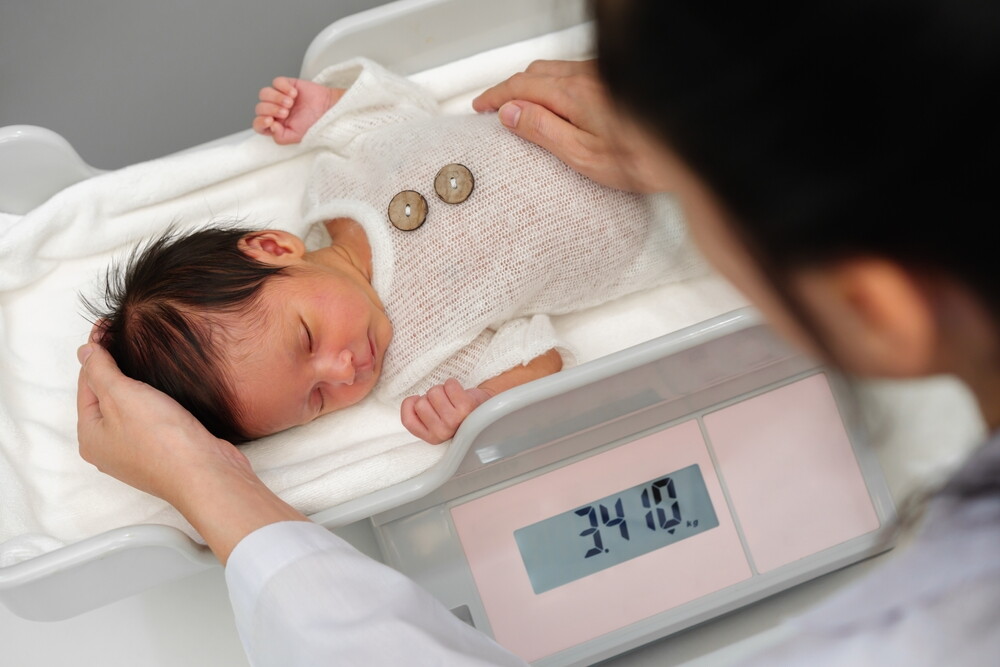 Baby under a year old asleep on a weighing scale during growth chart checkup.