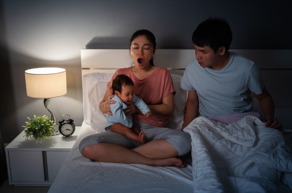  A sleepy mother wakes up her husband, and passes her crying baby to him bed.