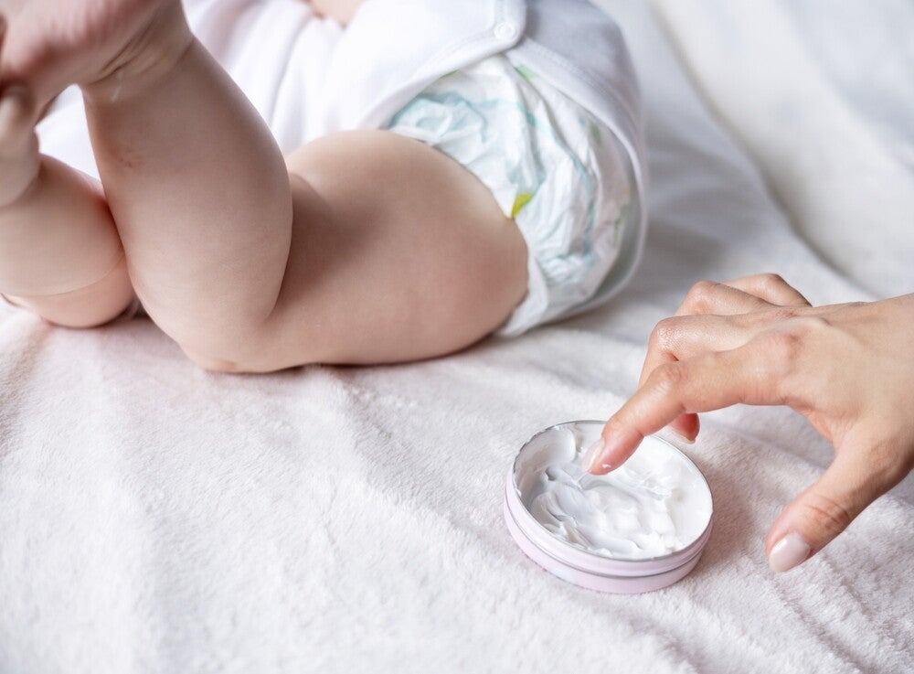  Close-up photo of a mom’s hand getting cream to apply to a baby. 