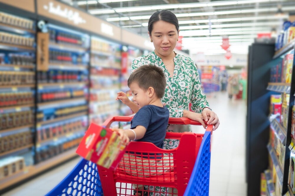 Shopping Asian mom looks on as her son drops a food item on the grocery cart. 