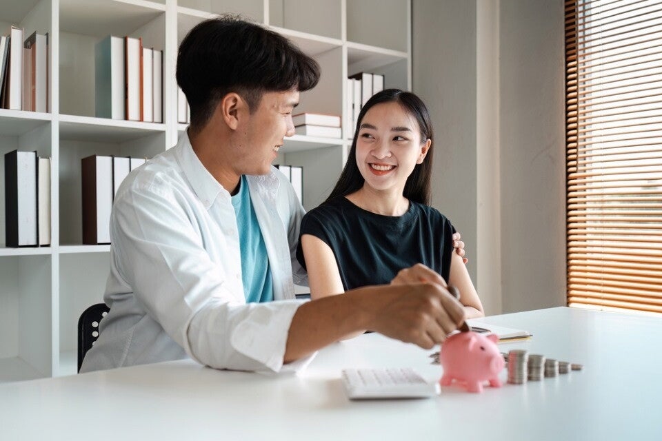 A young couple discussing financial savings and bills at home with piggy bank and calculator on table.