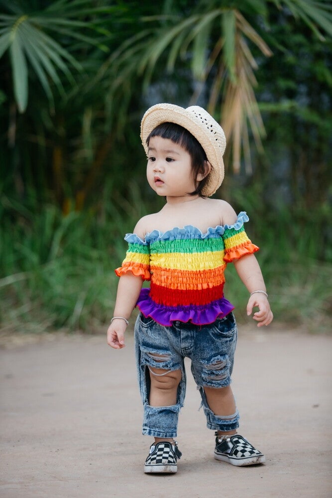 A portrait of a young Asian girl wearing a colorful top, distressed jeans, and a hat. 