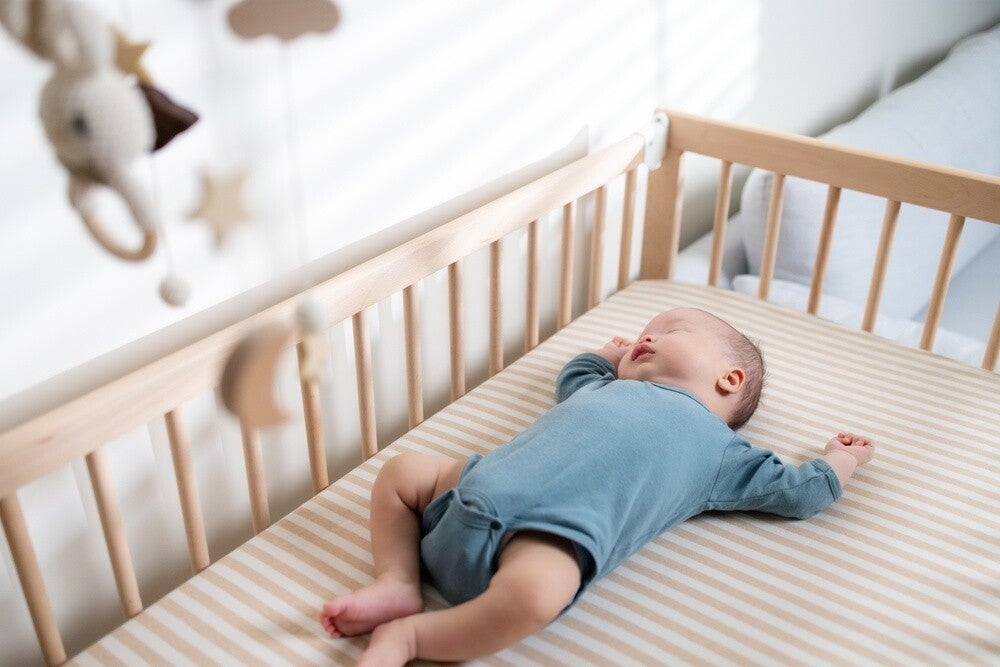Baby in onesie sleeping inside wooden crib.
