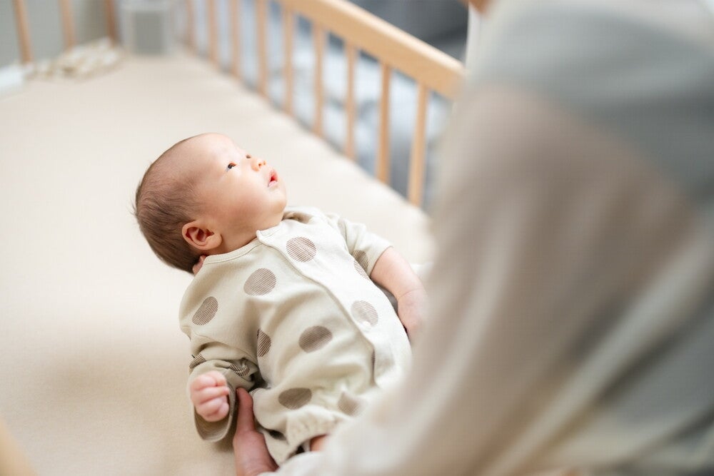  A blurred and cropped photo of a mom’s shoulder as she holds her baby and places him in the crib.