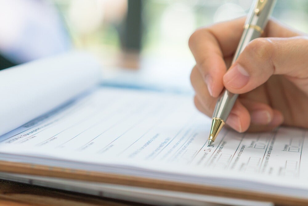 A hand holding a pen over an application form for a solo parent ID.