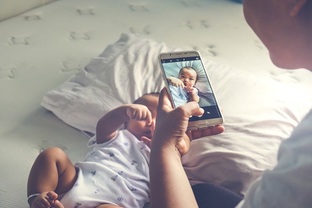 Asian mom takes a photo of her baby with her mobile phone's camera.