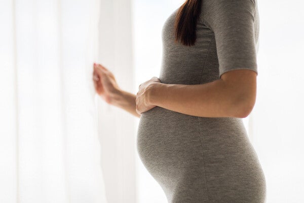 Side view photo of a pregnant woman in a stretchy dress showing off her baby bump.