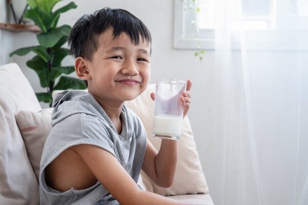 Smiling Asian boy drinking a glass of milk on the sofa at home.