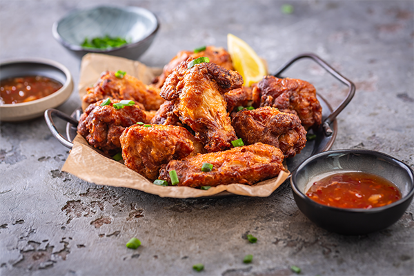 Photo of a plate of spicy Thai chicken wings with hot dip and green onions.