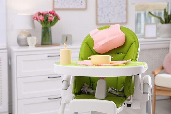 A high chair with baby plateware and utensils on the tray and silicone bib on the backrest.