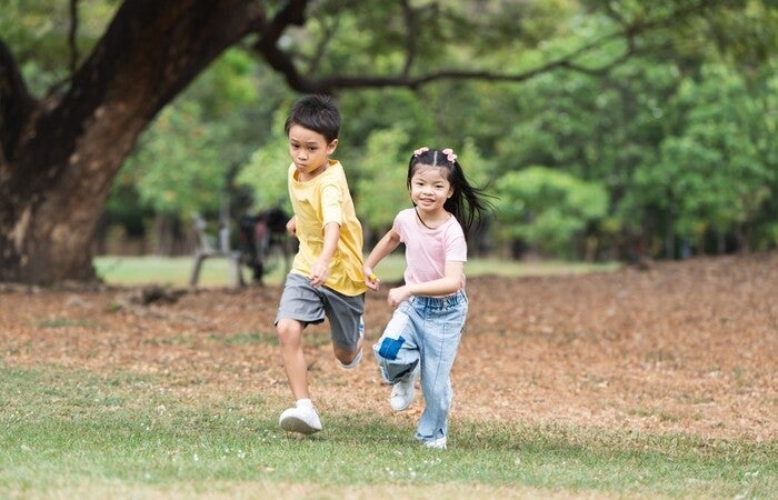 Two Asian children with different heights go running in a park. 