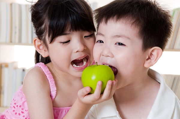 Two Asian siblings under the age of 7 try to bite into a green apple