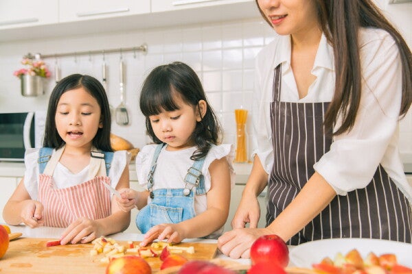 Two little Asian girls helping their mom prep fruits for their baon.