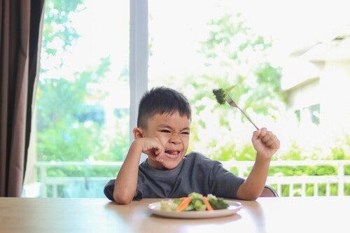 Unhappy Asian boy looking at his vegetables in disgust, not wanting to eat it