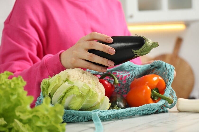 Close-up pic of a woman’s hands taking eggplant out from string bag at light marble table.