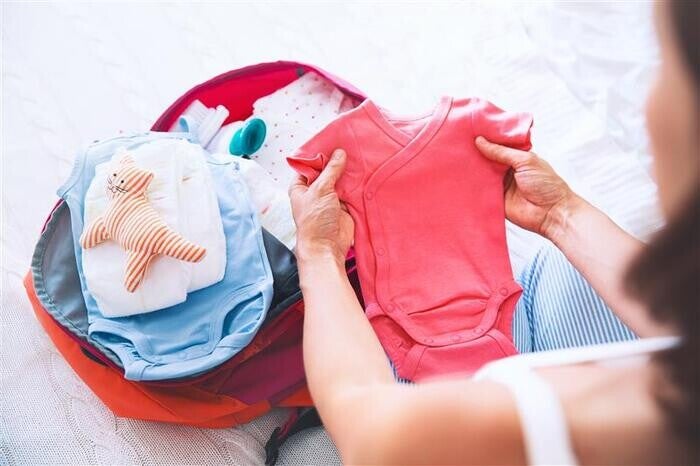 Woman packing baby clothes in bag.