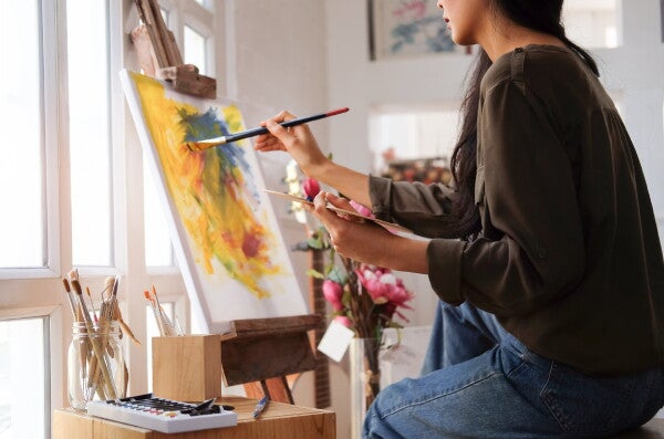 Woman in jeans and brown shirt painting on a canvas at home