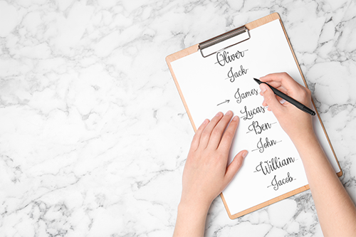 Woman choosing baby name at white marble table, top view