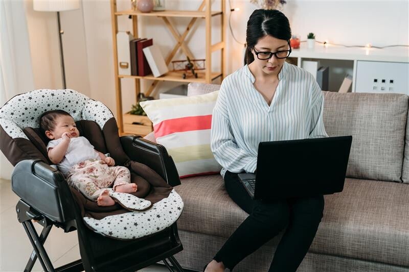 Working Asian mom with a laptop with baby next to her in a rocker
